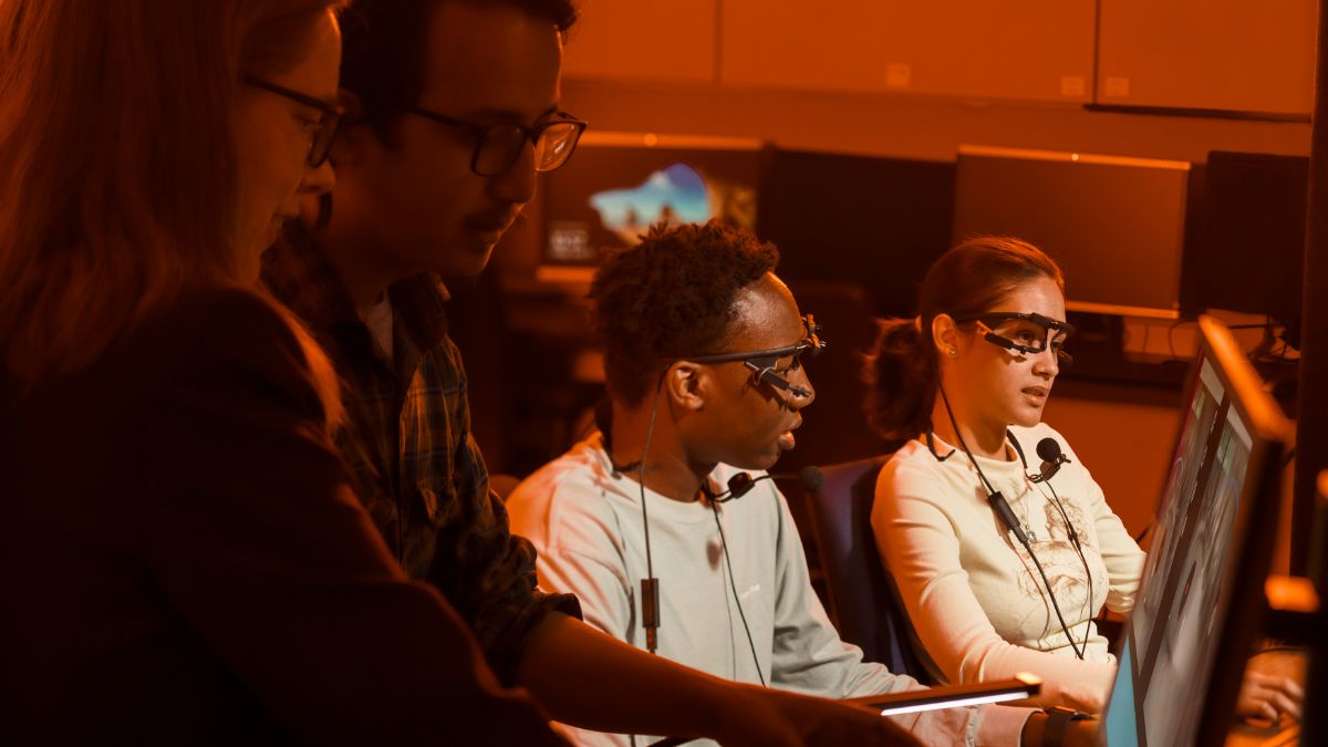 A group of people wearing headsets and glasses work together in a dimly lit environment.