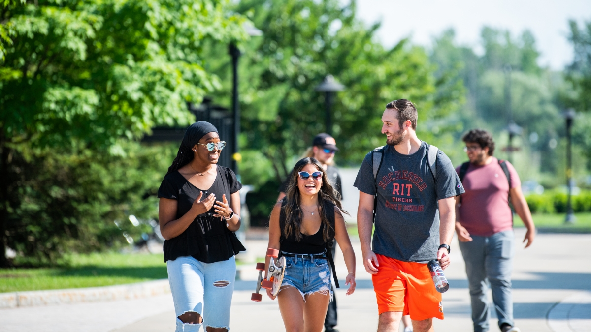 A group of students walks along a sunny path lined with trees, engaging in a lively conversation.