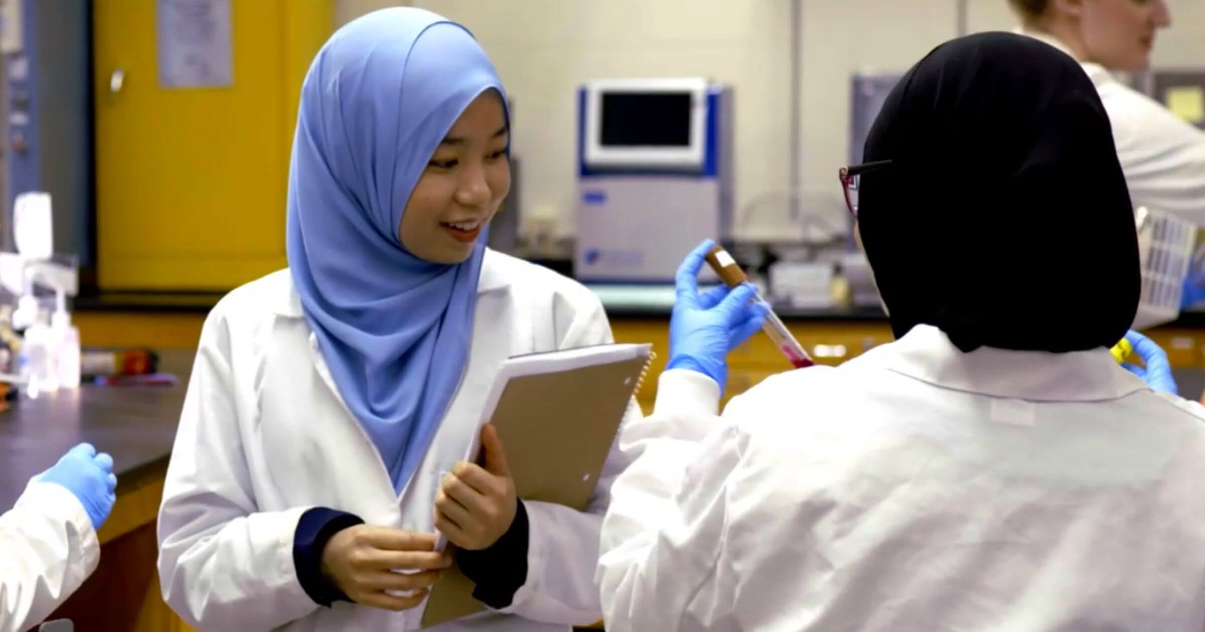 Students working in a lab, wearing lab coats.