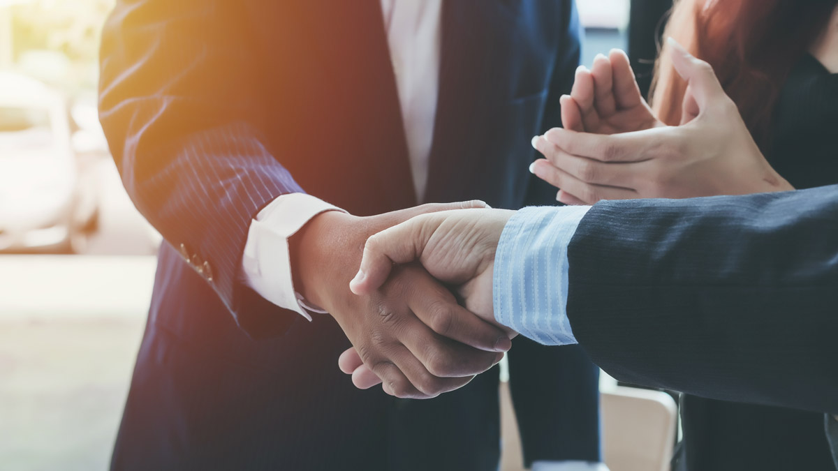 Two hands of people wearing suits shake hands.