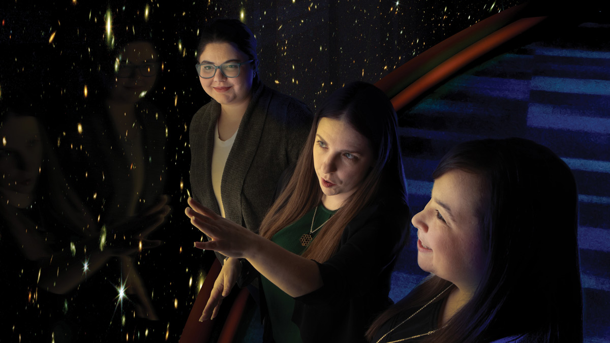 Three people look at a large projection wall of stars.