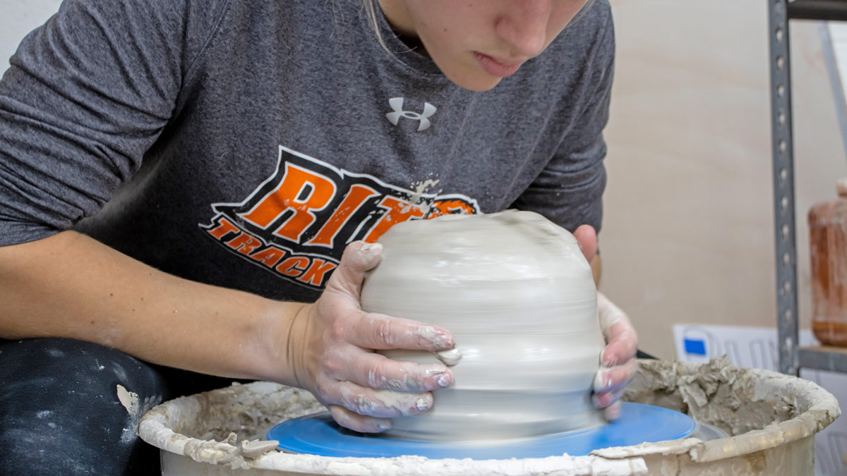 A student works at a wheel centering a large amount of clay.