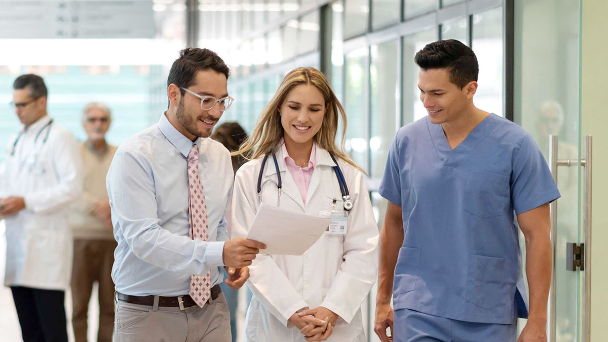 A doctor walks down a hallway with two other people.