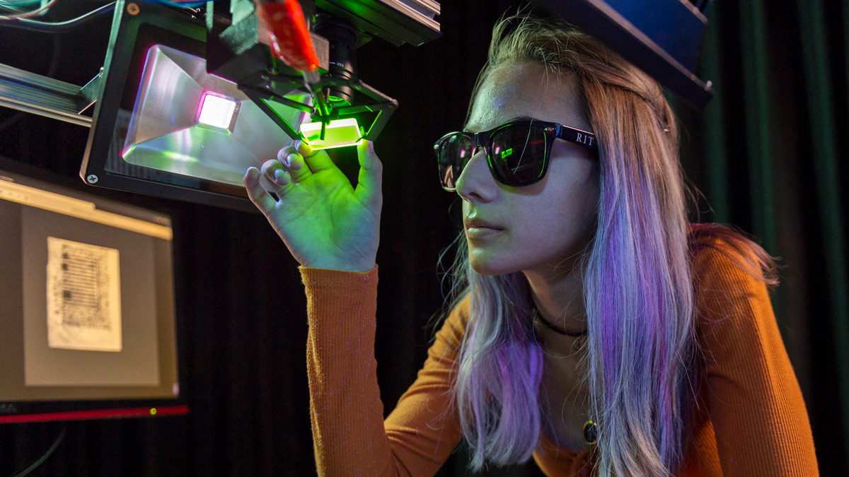 A student wearing sunglasses looks at something under a green light.