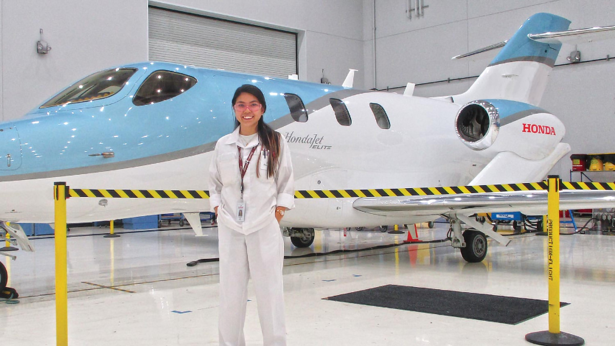 A student stands in front of an airplane with the Honda logo on it.