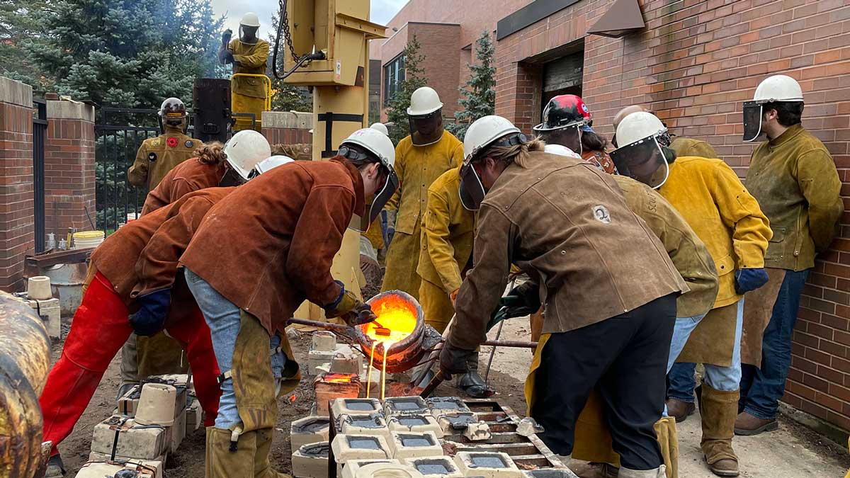 Students wearing protective gear pouring molten liquid into forms.