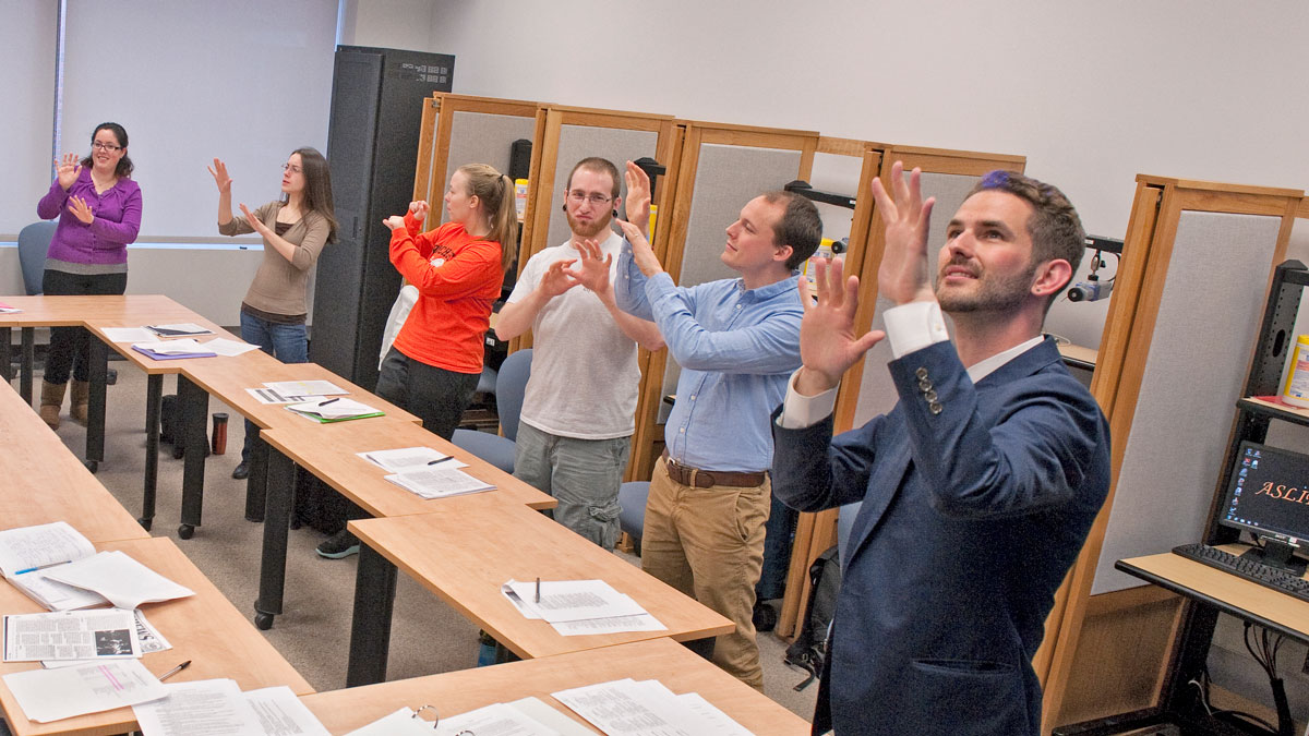 A group of people standing around a table doing ASL.