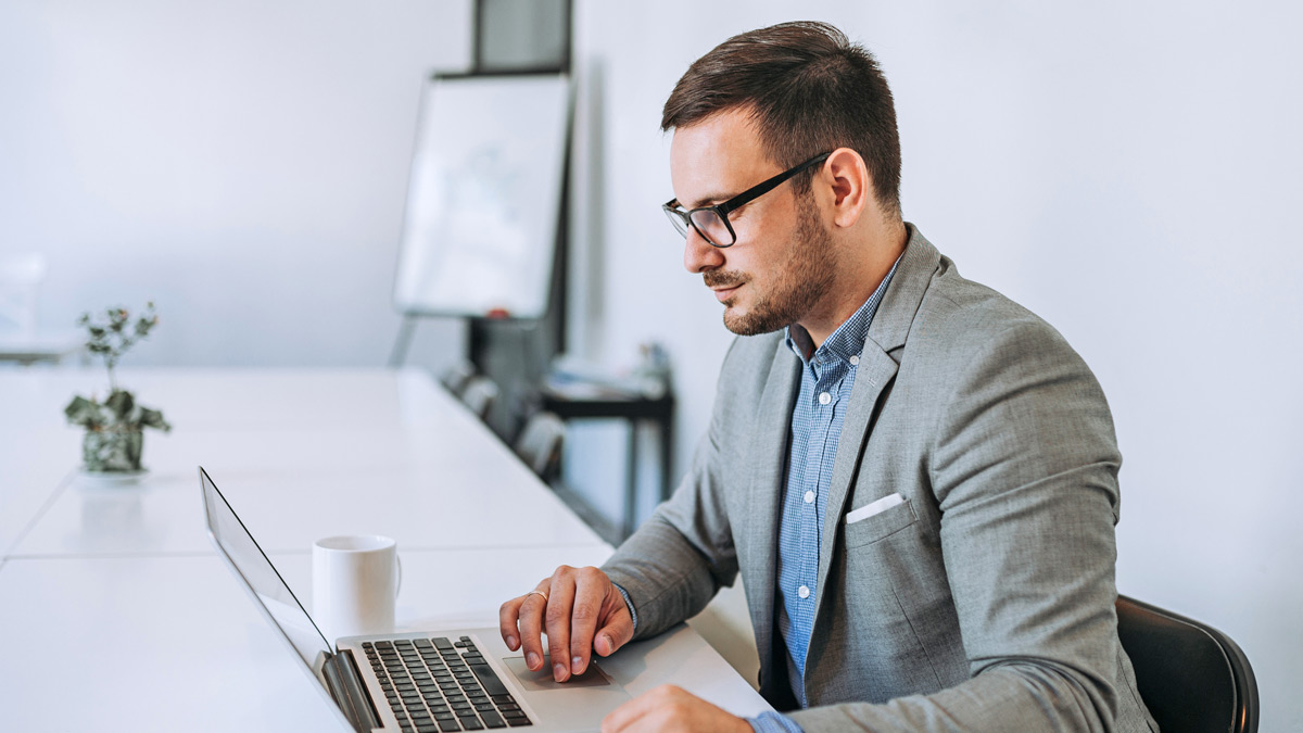 A man sits at a table using a laptop.