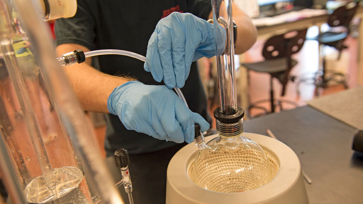 Hands wearing light blue gloves work with glass bowl.