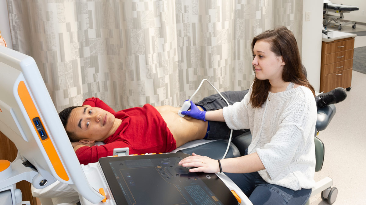 A woman using an ultrasound wand on a man who is looking at the monitor.