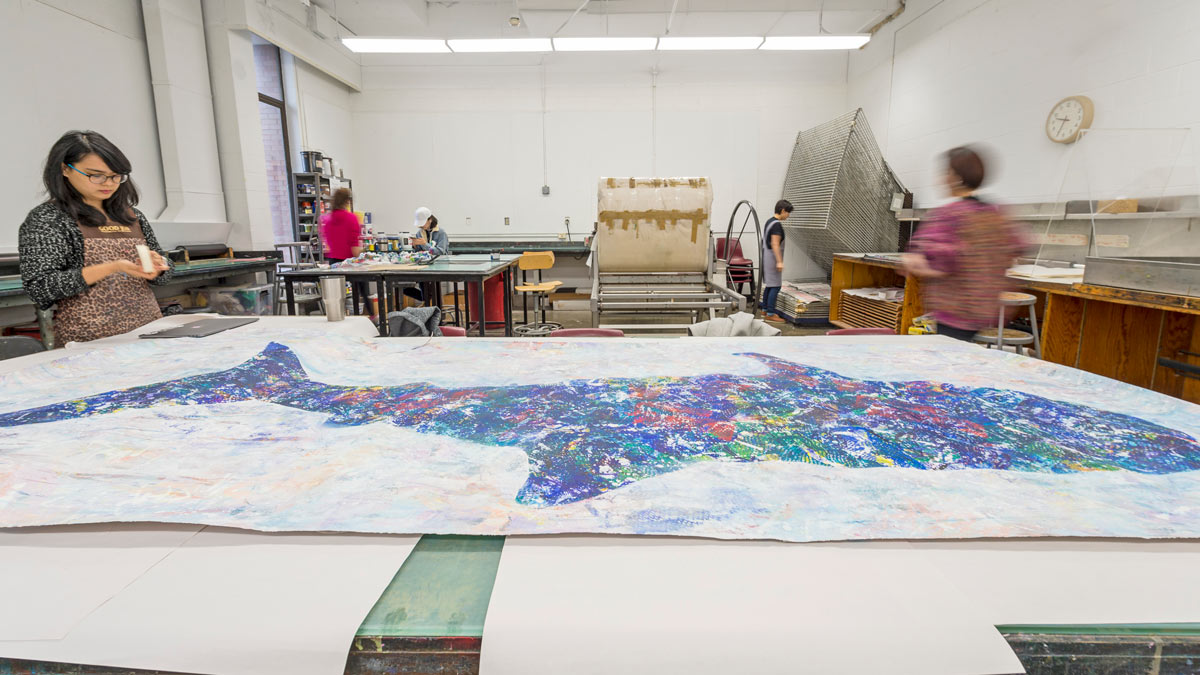 A large, textured artwork in the shape of a whale lays across studio tables.