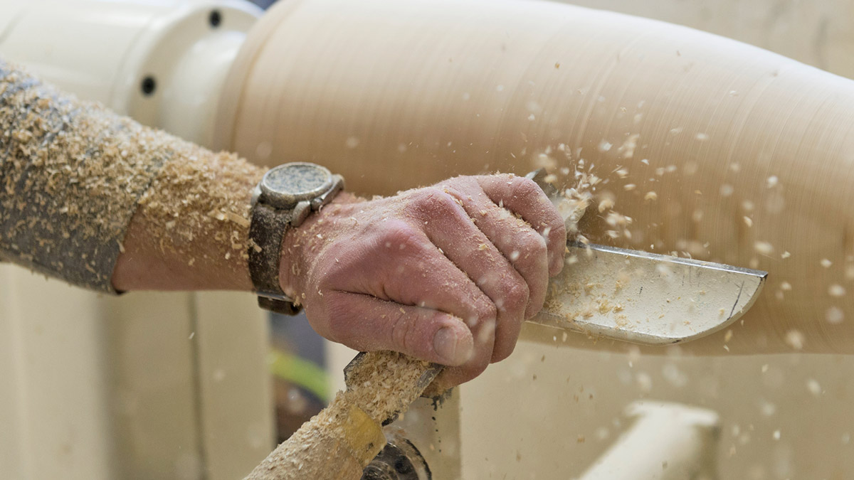 Close up of sawdust covered hands carving wood.