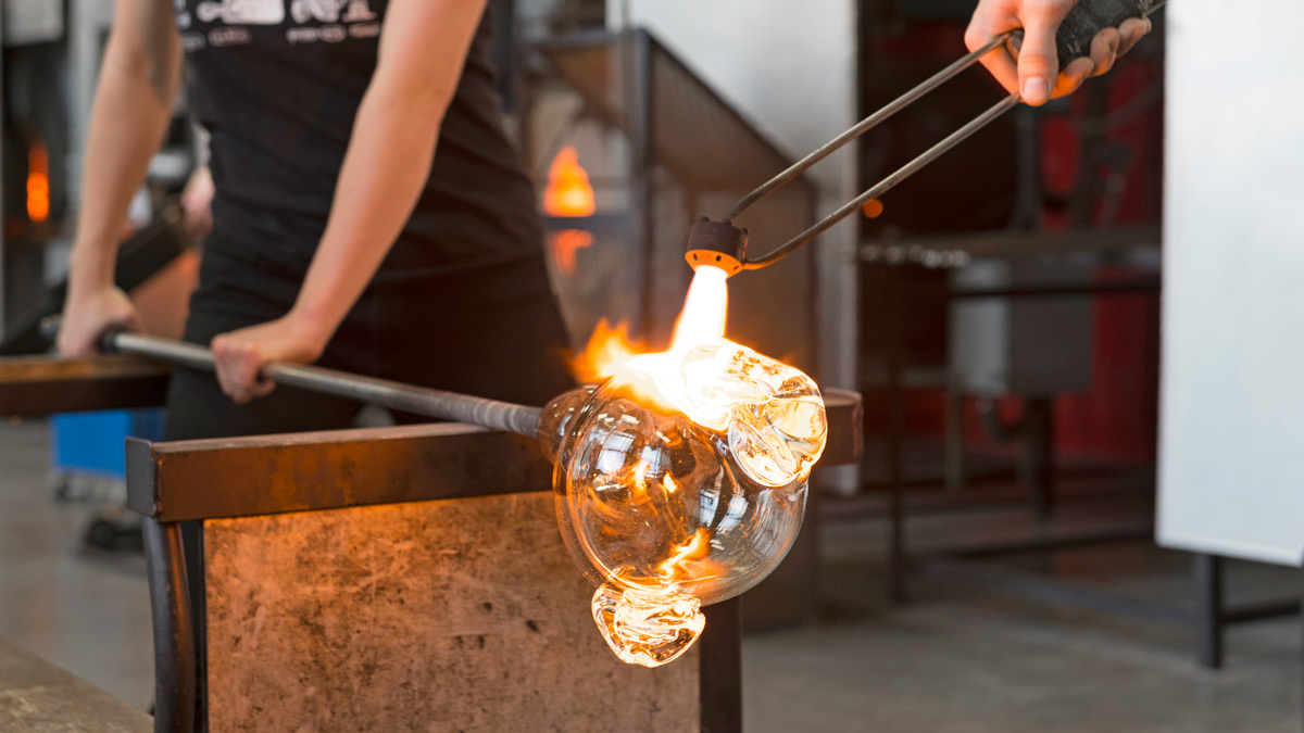 Hands holding rod of blown glass.