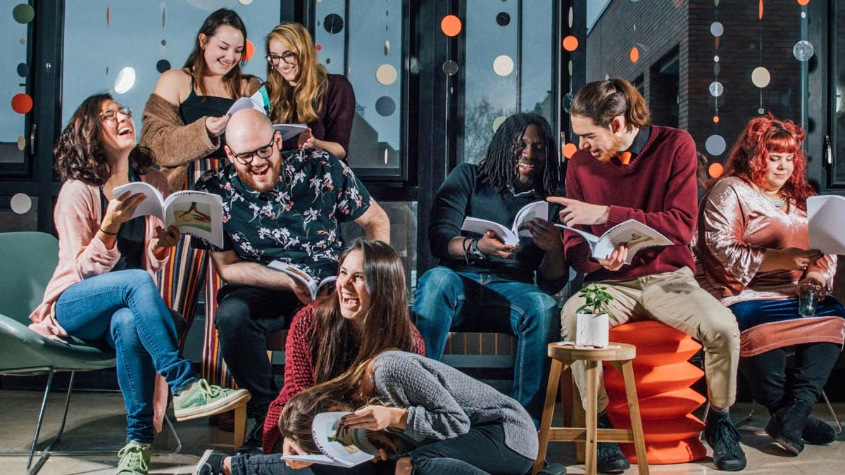 Graphic design students sit on uniquely designed chairs while looking at copies of a magazine.