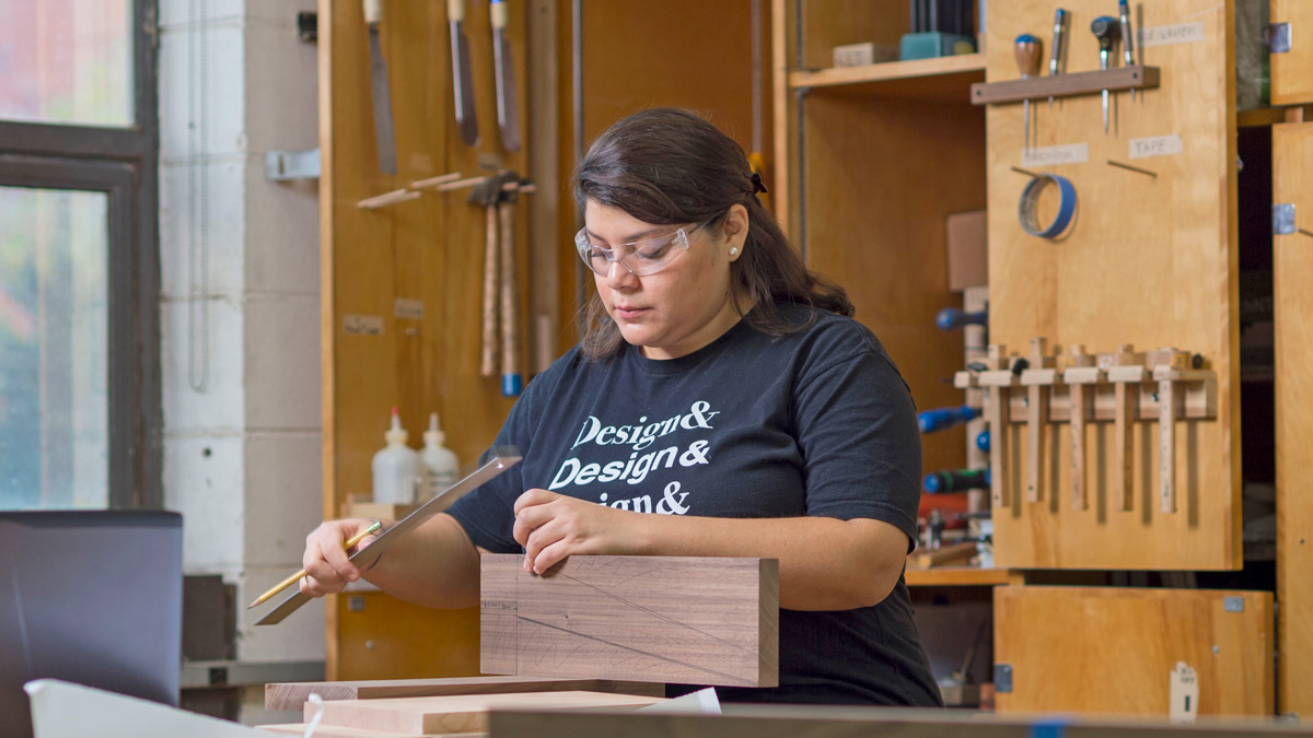 Student with ruler and pencil in hand makes measurements on a piece of wood.