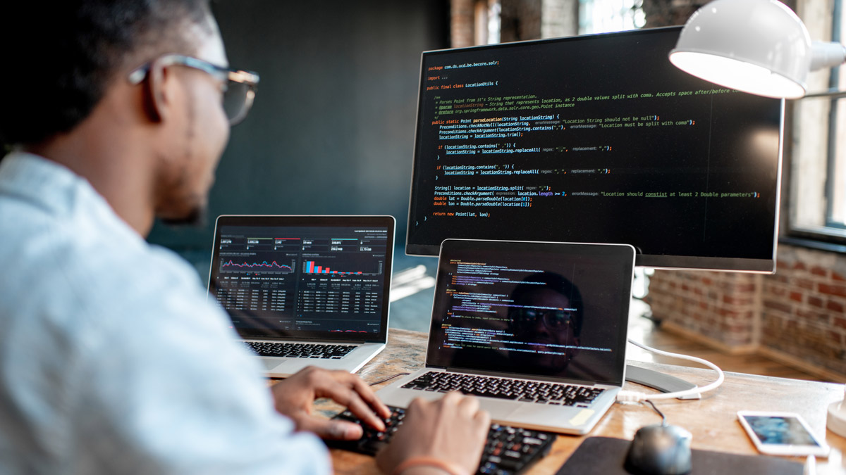 Person working on multiple laptops with code and graphs.