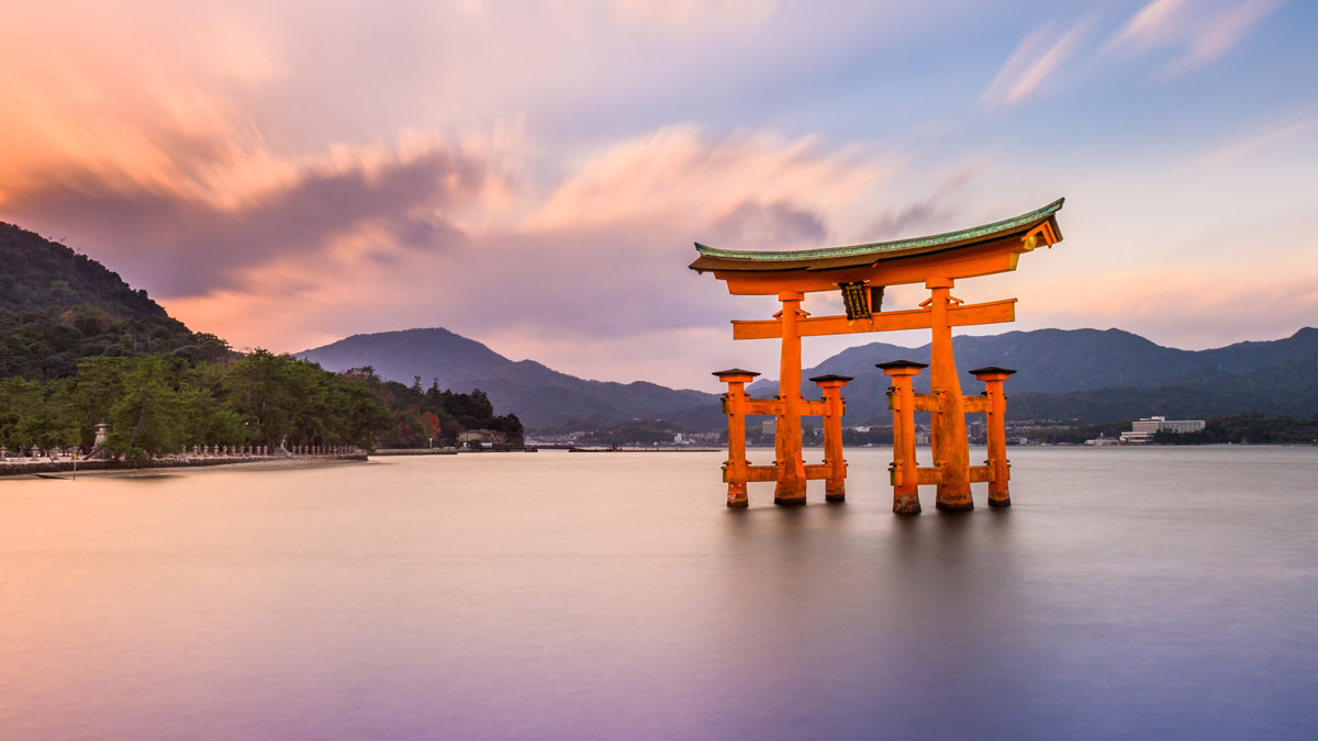 A Japanese 'torii' gateway sits in the water with mountains in the background.