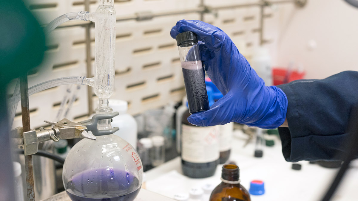 Blue-gloved hands hold a capped tube of fizzy, dark liquid.