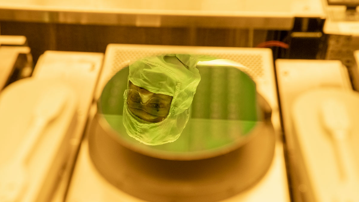 A student in a bunny suit and goggles is reflected in a wafer.