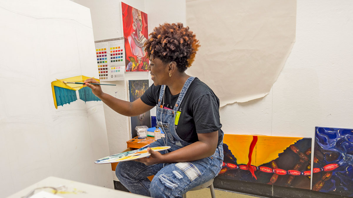 In a studio space, a student works on an painting of a room with several doors or lockers.