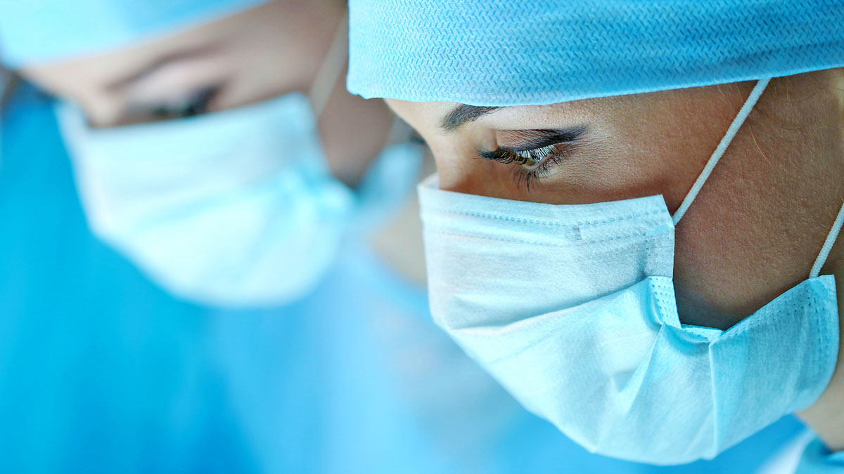 A close-up photo of 2 people wearing scrubs and medical masks.