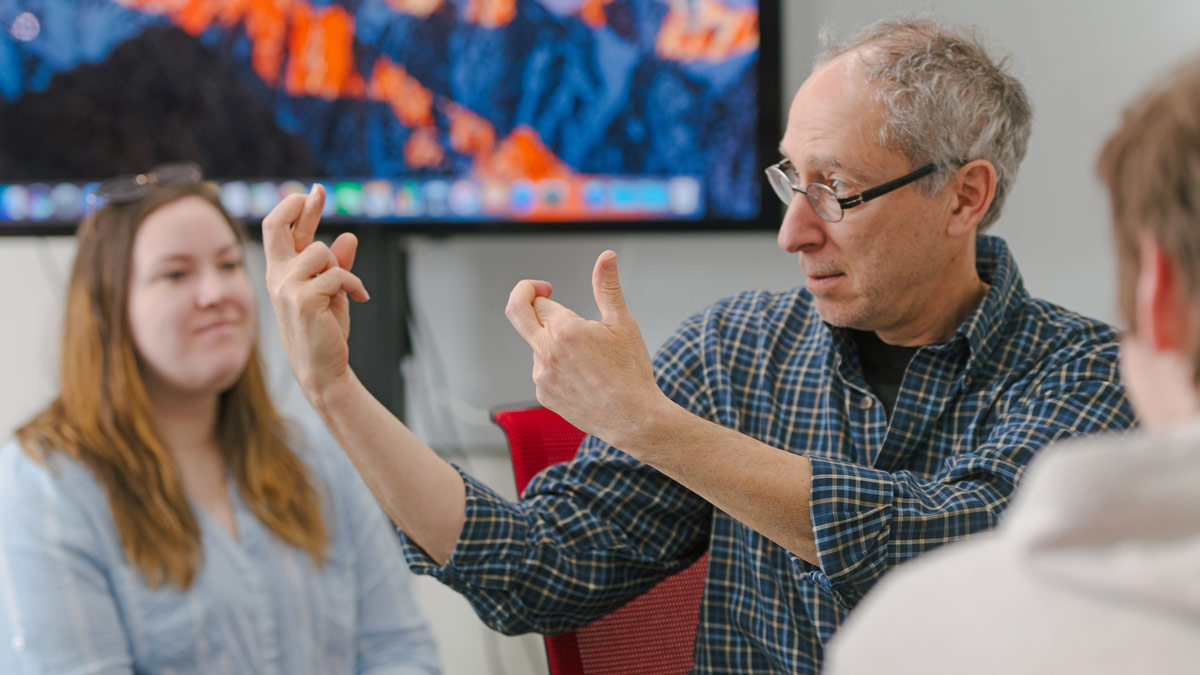 Professor signs with the R handshape to a group of students.