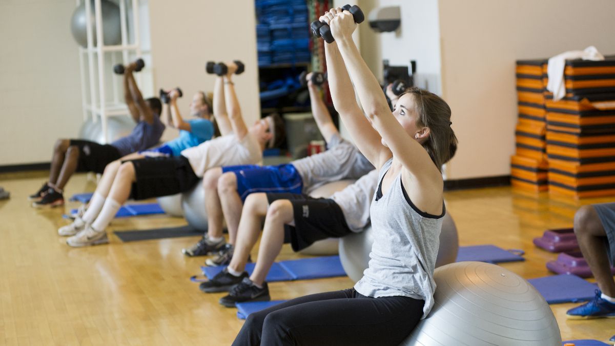 A group of students lift hand weights in a workout space.