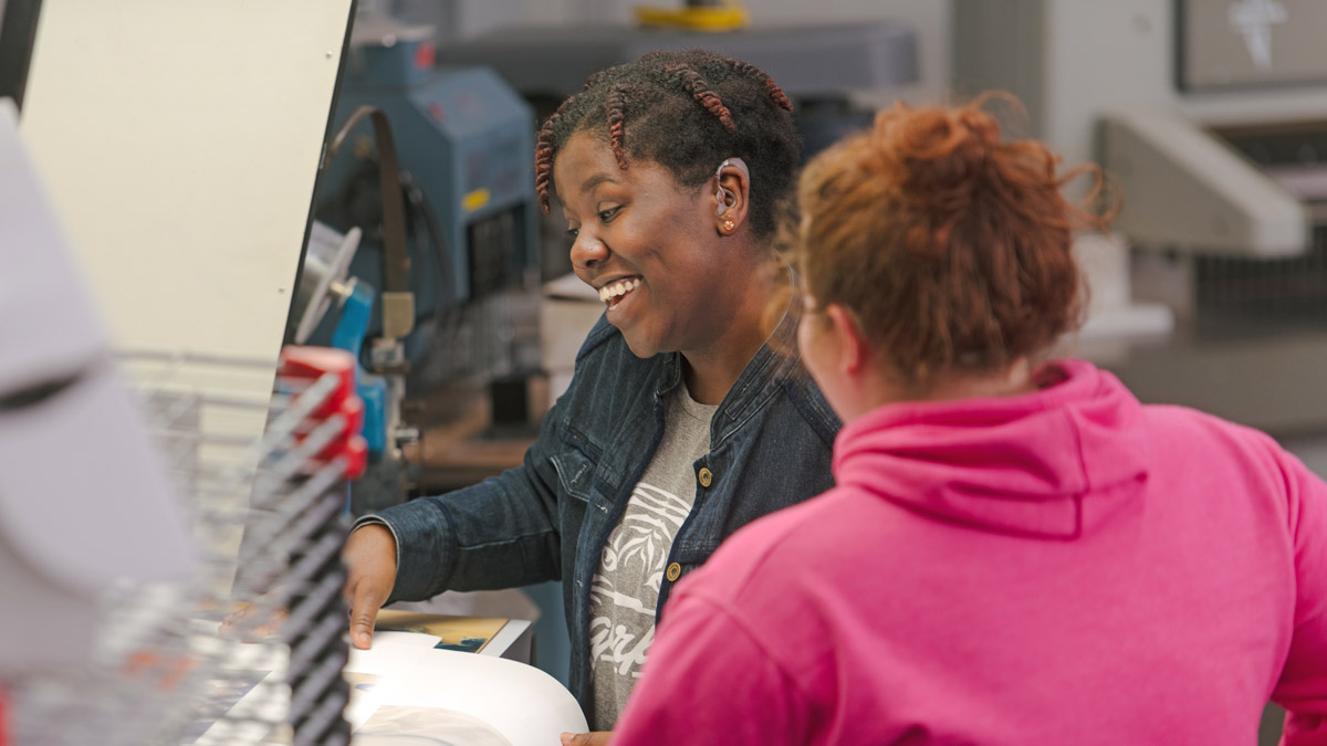 Two students laughing in front of a light table station.