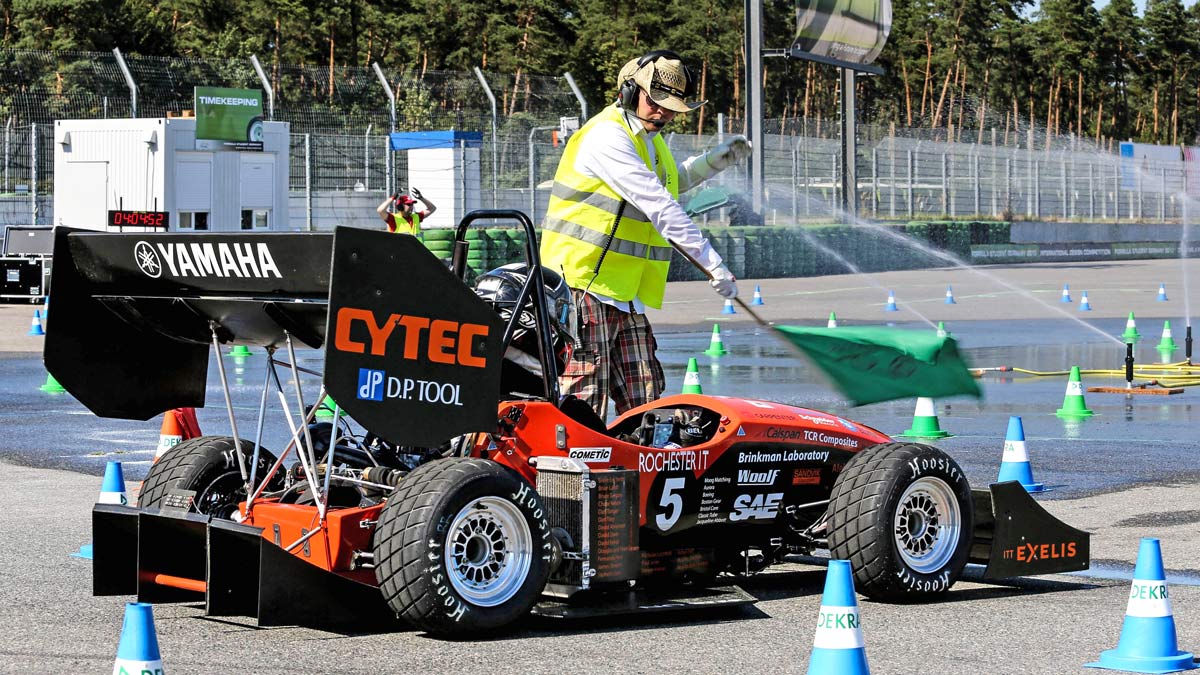 RIT's Formula SAE car with a person waving a green flag in front of it.