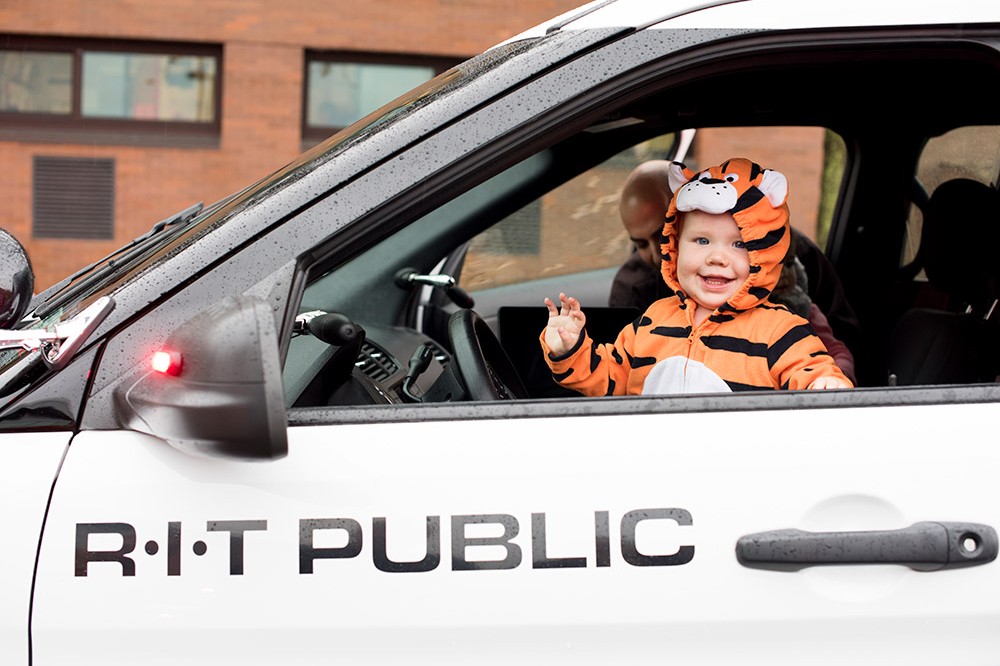 Child in tiger costume sits in front seat of RIT Public Safety car.
