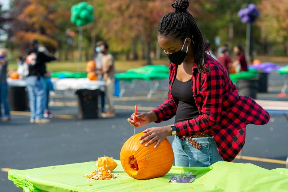 Student carves pumpkin on table in parking lot