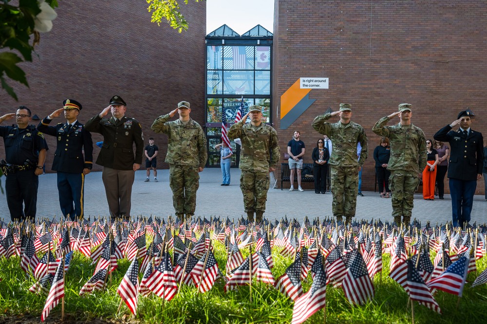 members of the armed forces stand saluting in front of a display of american flags.