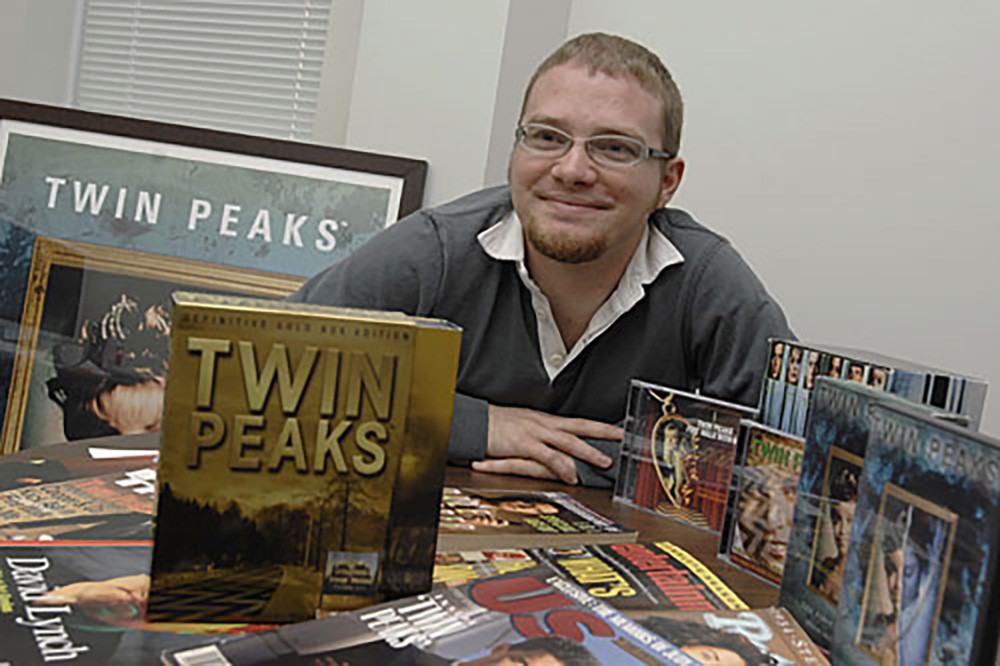 Jared sitting a table with various Twin Peaks box set, magazines, and memorabilia around him.