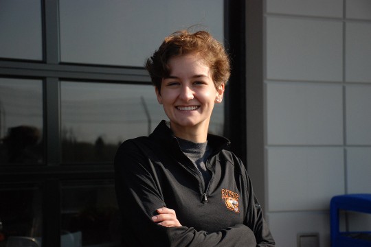 a female student in black R I T cothing appears with their arms crossed in front of a window.