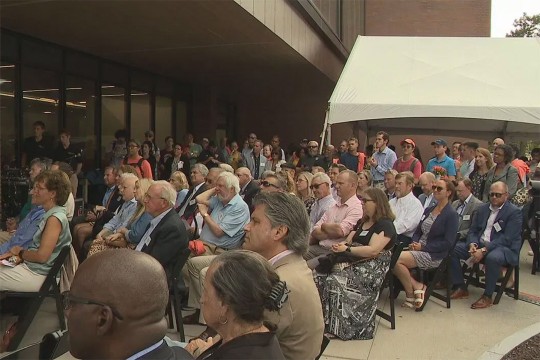 'a crowd of people sit and listen to speakers outside Max Lowenthal Hall.'