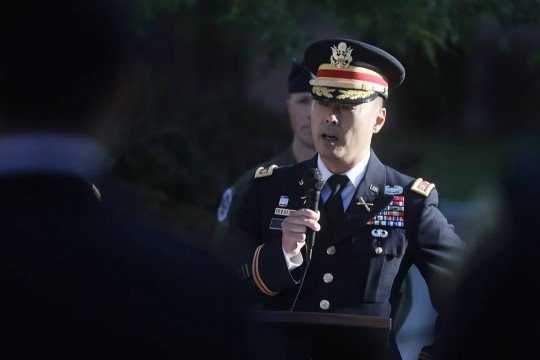 'a man in military dress speaks in to a microphone in an outdoor space.'