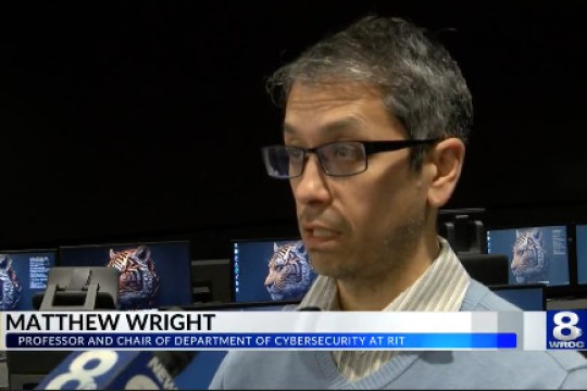 Matthew Wright stands in front of a camera on TV with his name appearing below his face.