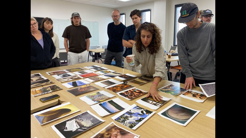 A group of artists look at photo prints spread out on a table.