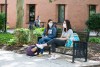 two students wearing face masks sitting on a bench outside.