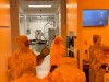 students in clean room uniforms stand in a research room.