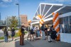 students gather outside a large white tent with orange and white balloons on either side of the entrance.