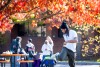 A young black student in a white shirt flips a hackey sack off his foot. In the background other students talk to each other under colorful trees.