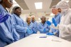 students in blue clean room suits stand around a table.