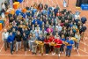 Large group of people gathered on an indoor track, many wearing business or company-branded attire and holding R I T Tigers signs, smiling at the camera.