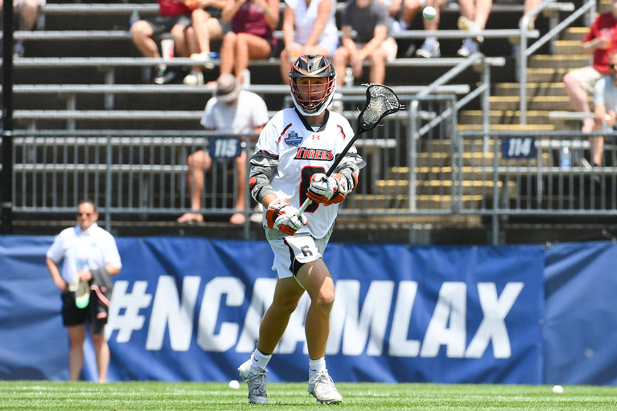 a lacrosse player on the field with bleachers behind them