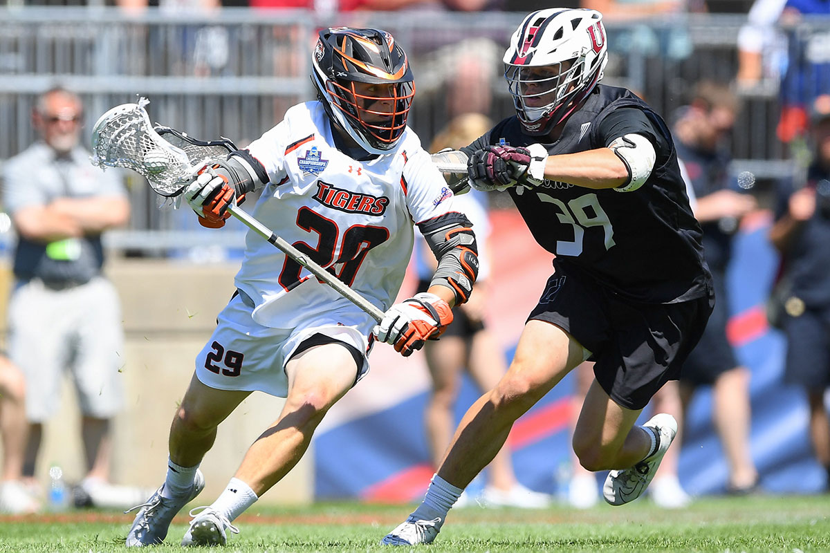 one lacrosse player chasing another that has the ball