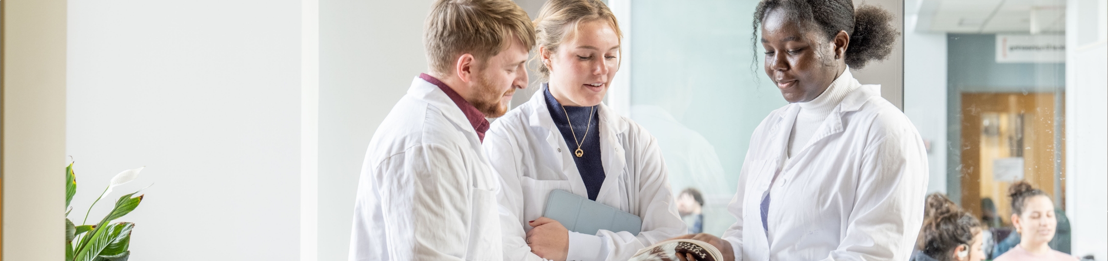 Three people wearing lab coats standing while reviewing some printed materials