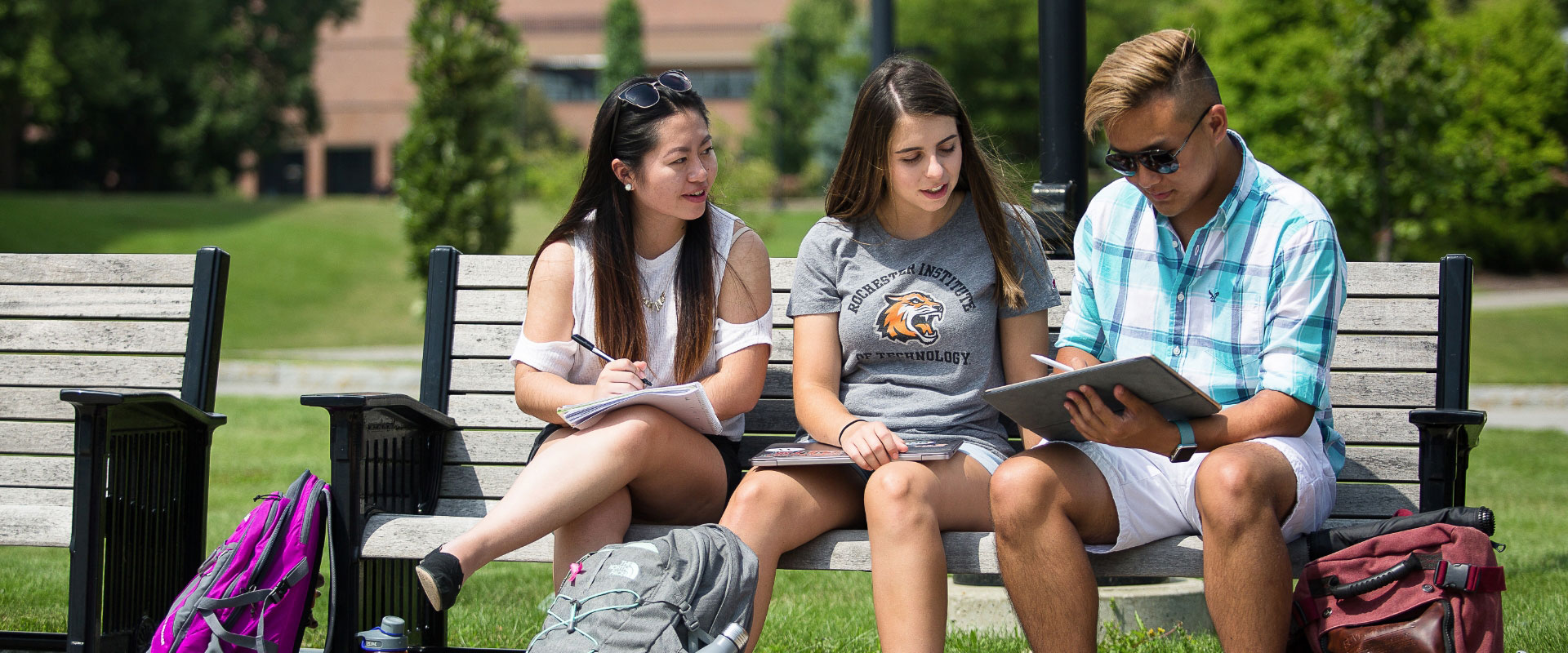 Three students sitting on a bench in Kodak Quad