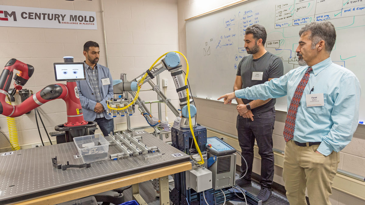 Students and professor work with mechanical robot arms.