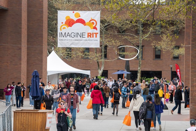 crowds of people are shown walking through campus with an Imagine RIT banner flying above them.